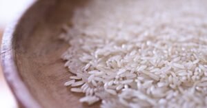 Close-up view of raw, uncooked rice grains on a rustic wooden plate. Perfect for culinary themes.